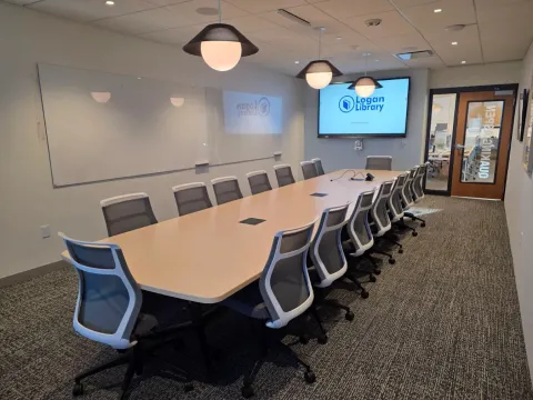 Photo of conference room with table, chairs, whiteboard, and monitor visible.