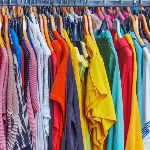 A bunch of shirts on hangers, hanging on a clothing rack.